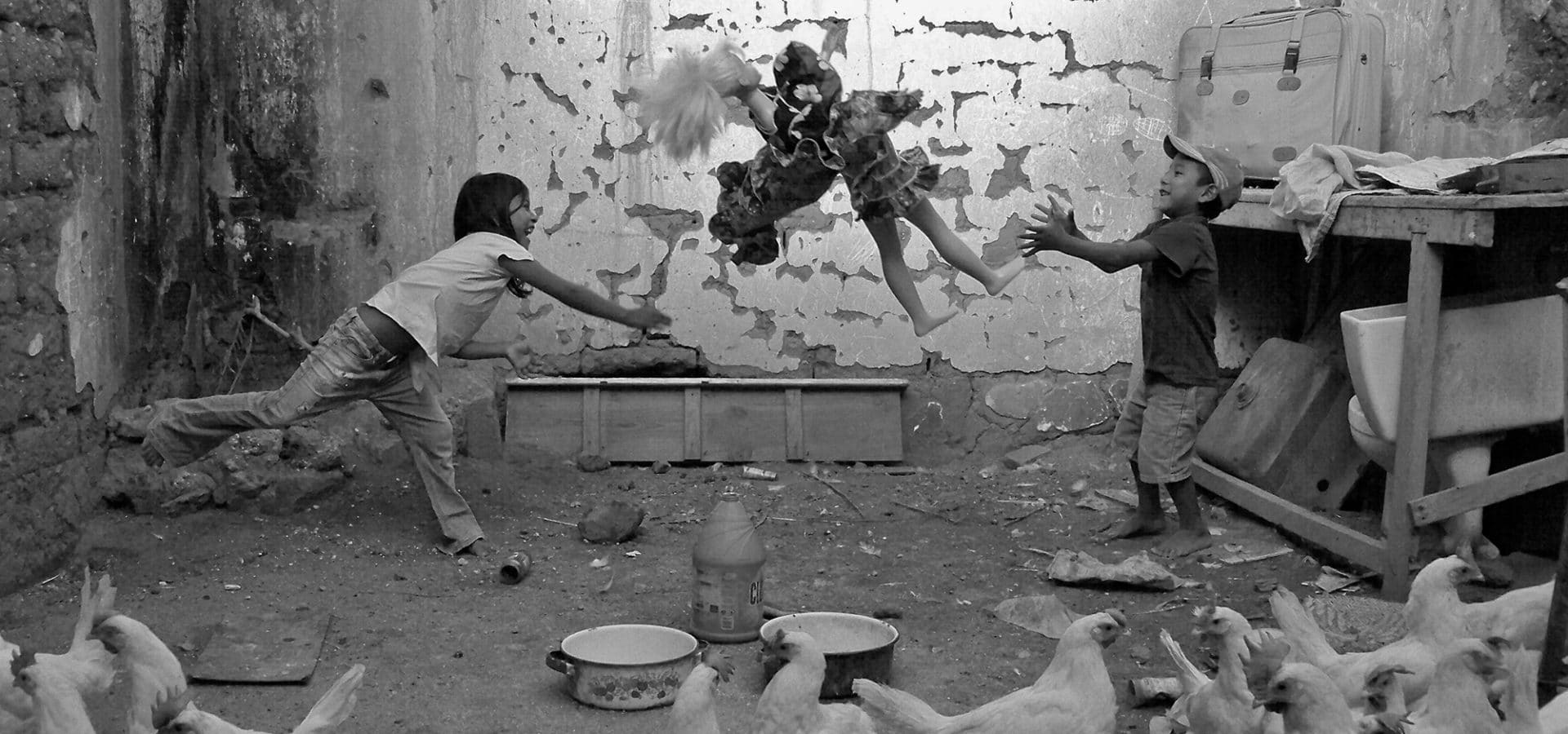 Joel Orozco, Beyond the Mask: Children inside a chicken coop, throwing doll in the air