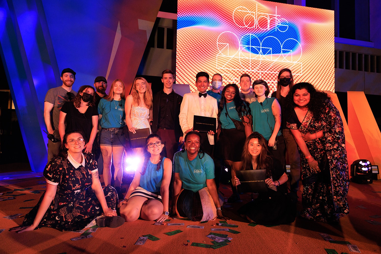 Production team members pose and smile for the camera on the graduation stage.