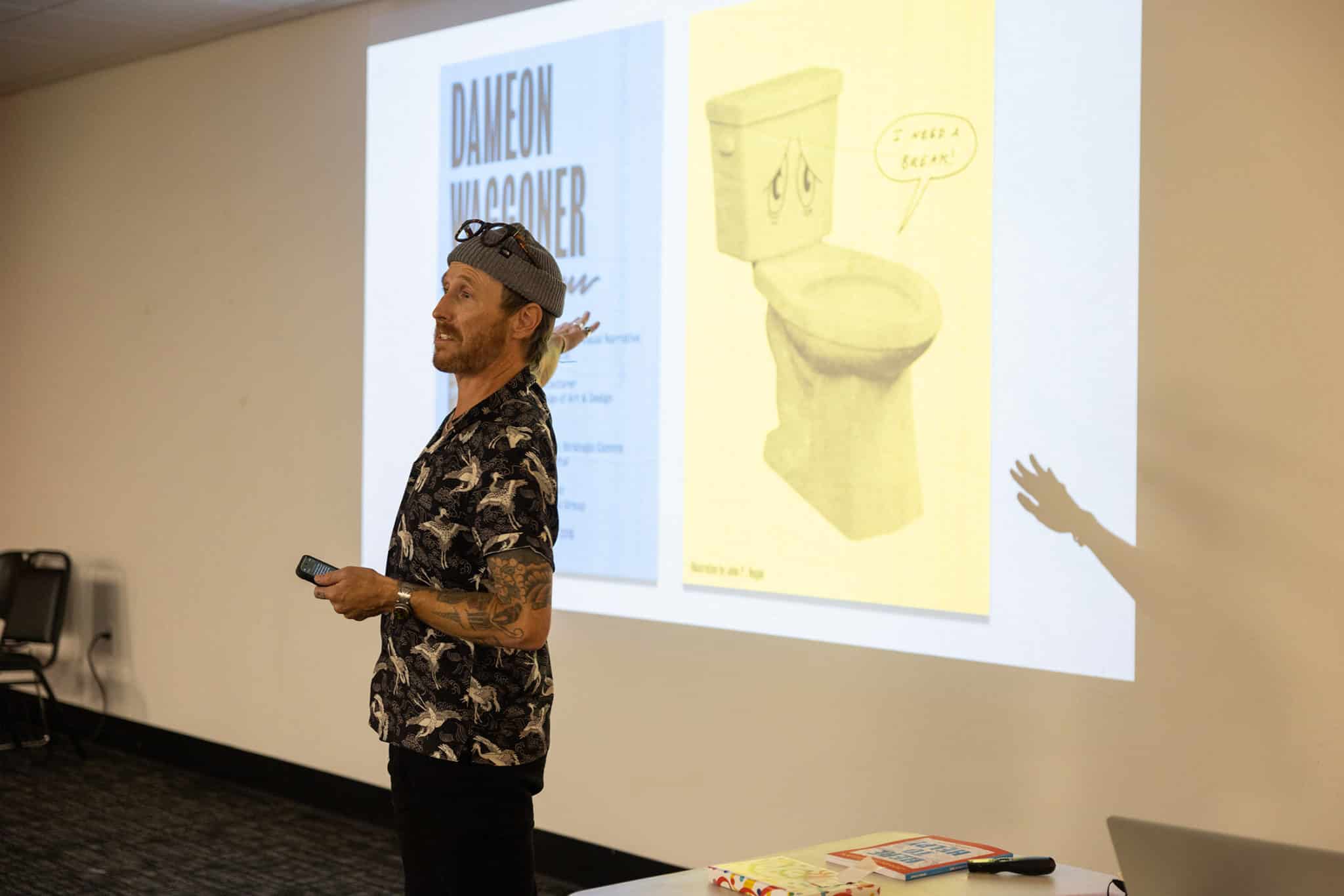 Man gestures behind him to a projected image of the Here to Help book cover.