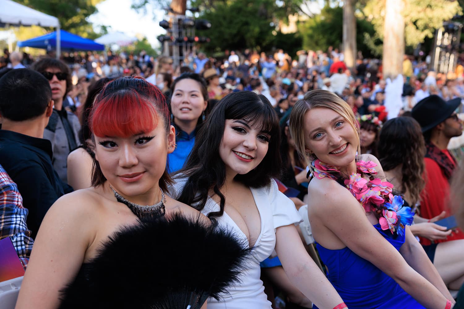 Three students smile at the camera while sitting outside for the ceremony.
