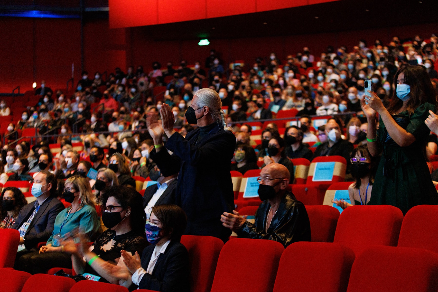 Attendees watch the stage (out of frame to the left), some standing and applauding.