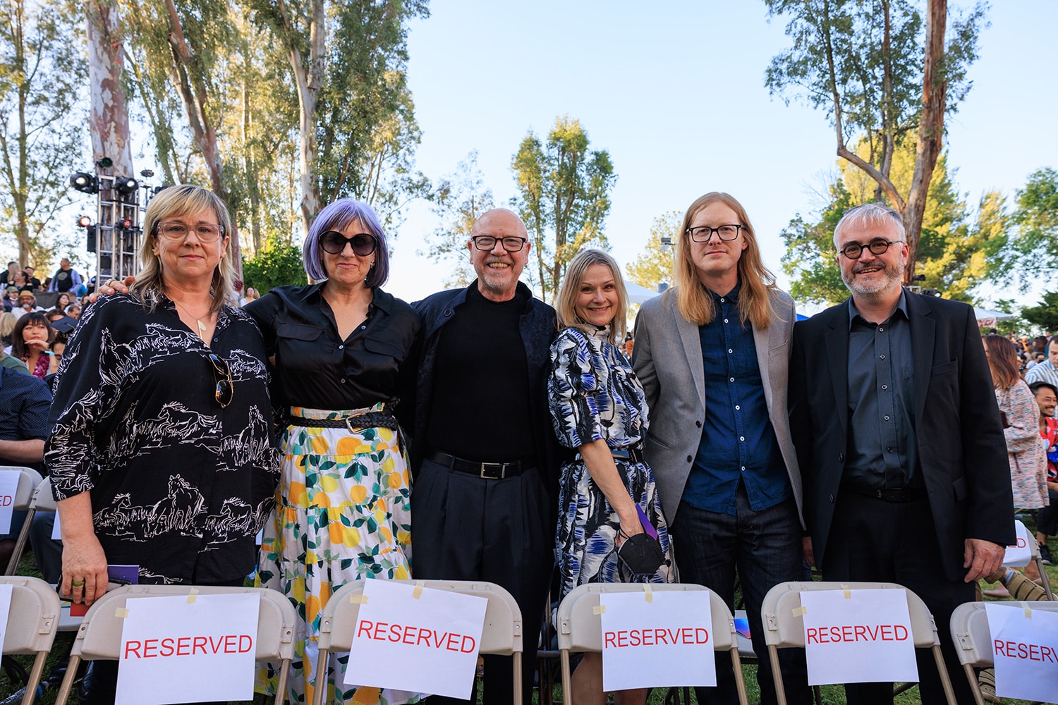 The six stand shoulder-to-shoulder and smile at the camera.