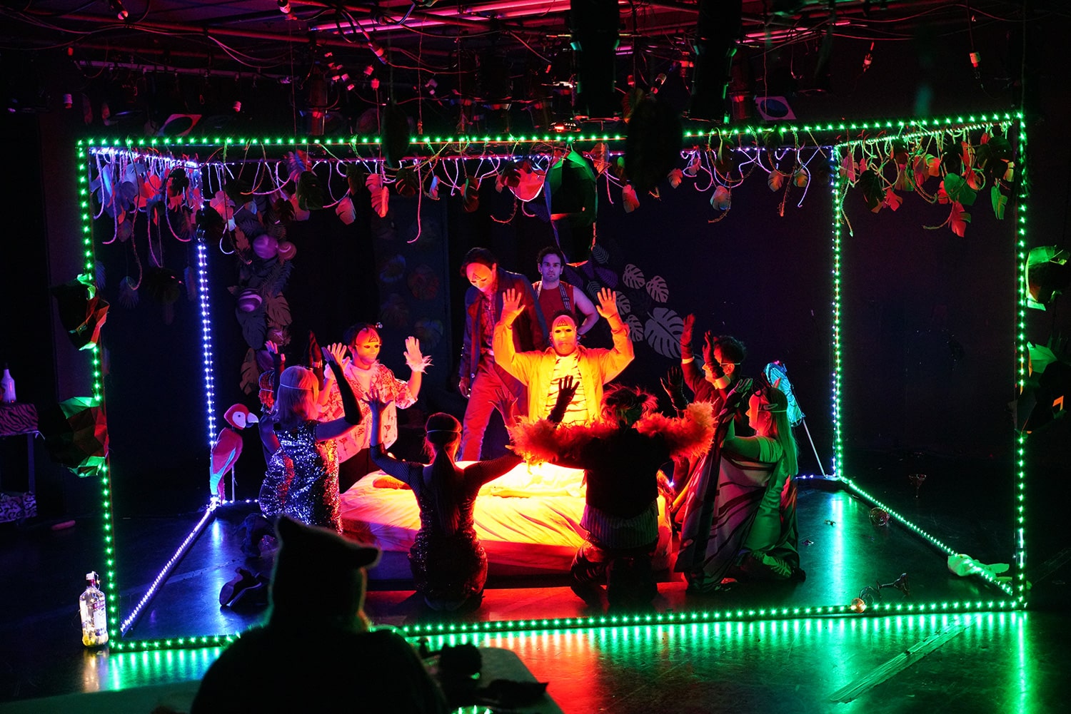 A group of people sit on stage in a cube formed by strings of green lights