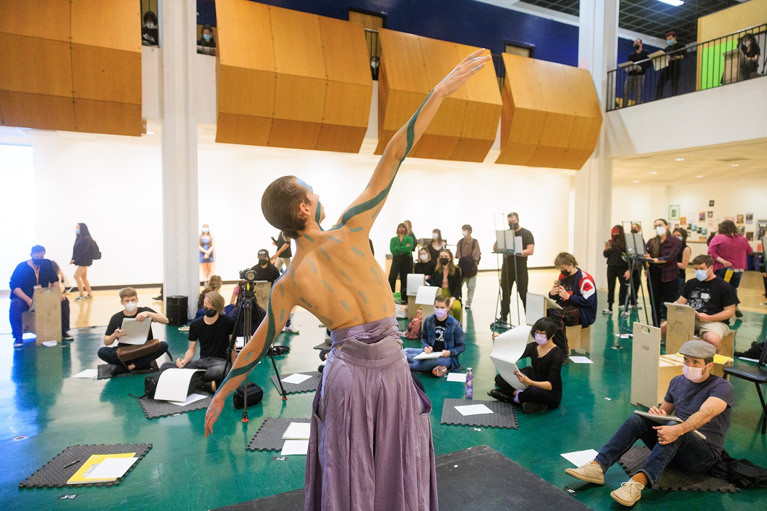 A dancer wearing body paint poses as artists, seated, observe and draw.
