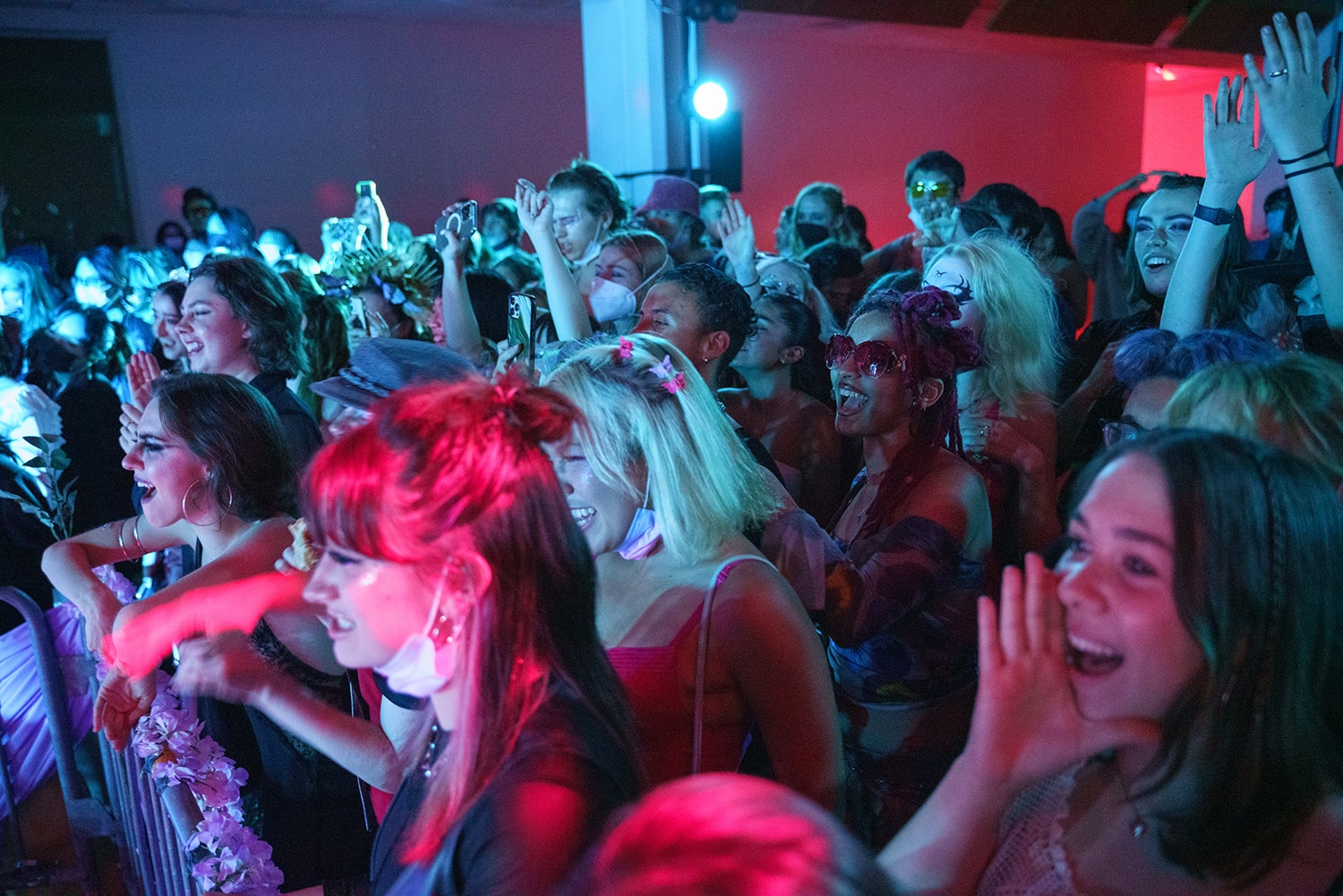 Blue and pink lights on students clapping and cheering behind a barricade.in