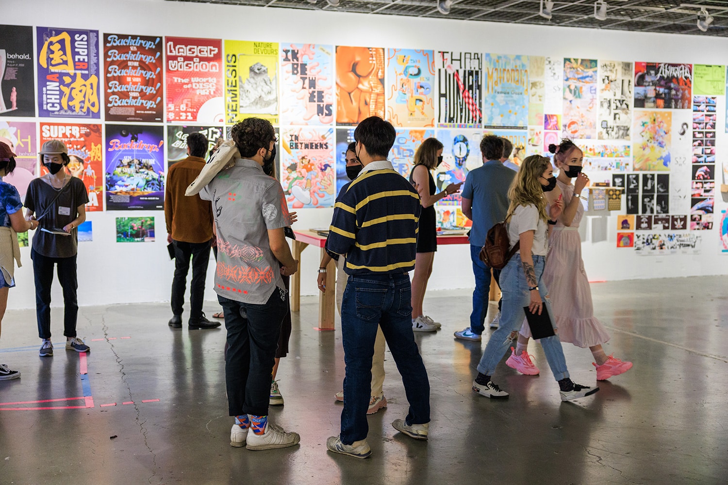 Students walk around and observe a gallery filled with graphic design posters.