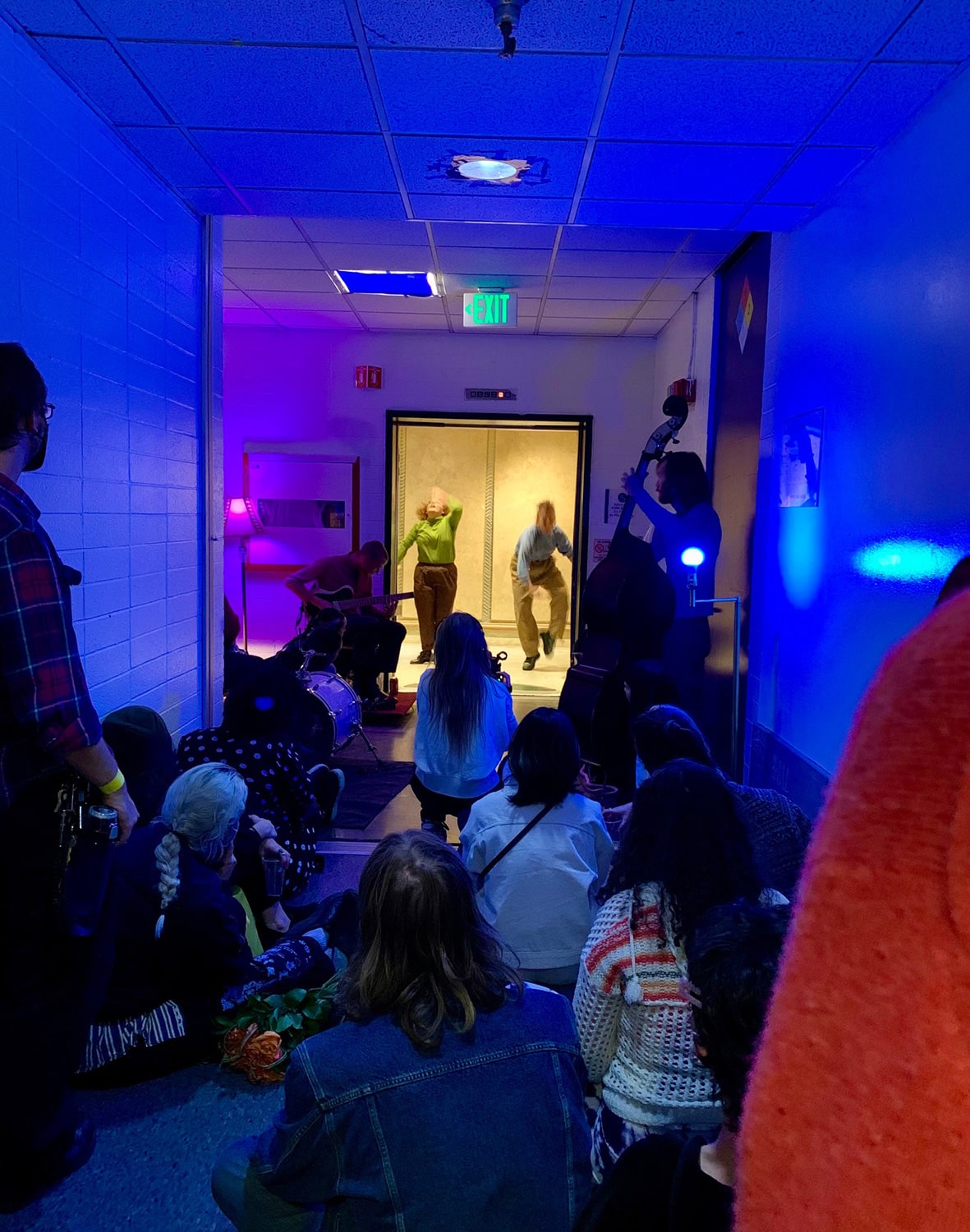Students sit in the blue-lit hallway to watch performers in the open elevator.