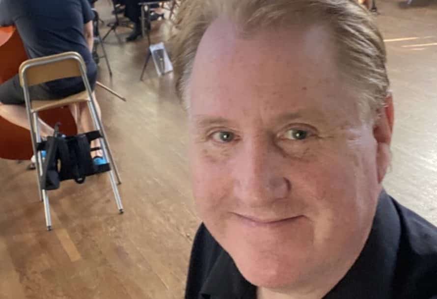 smiling man looking at the camera in front of a room of people