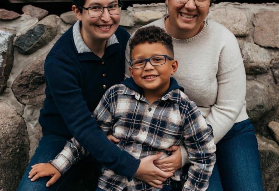 Alex Lewin and her partner smiling as they hold their son