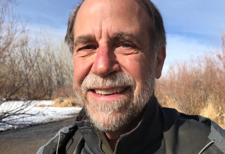 Bob Bassett smiles standing against blue sky and trees