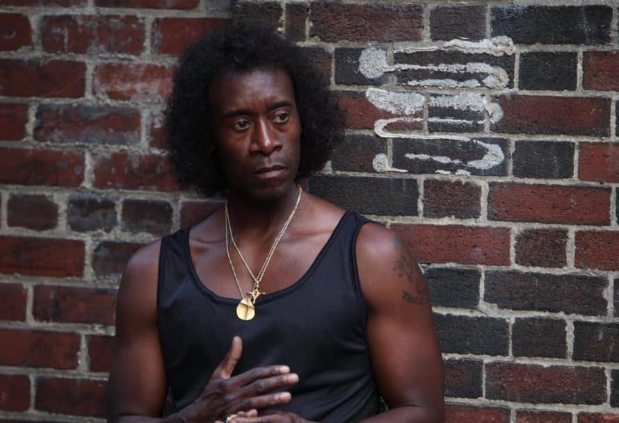 Don Cheadle as Miles Davis, in a black tank top, standing against a brick wall.