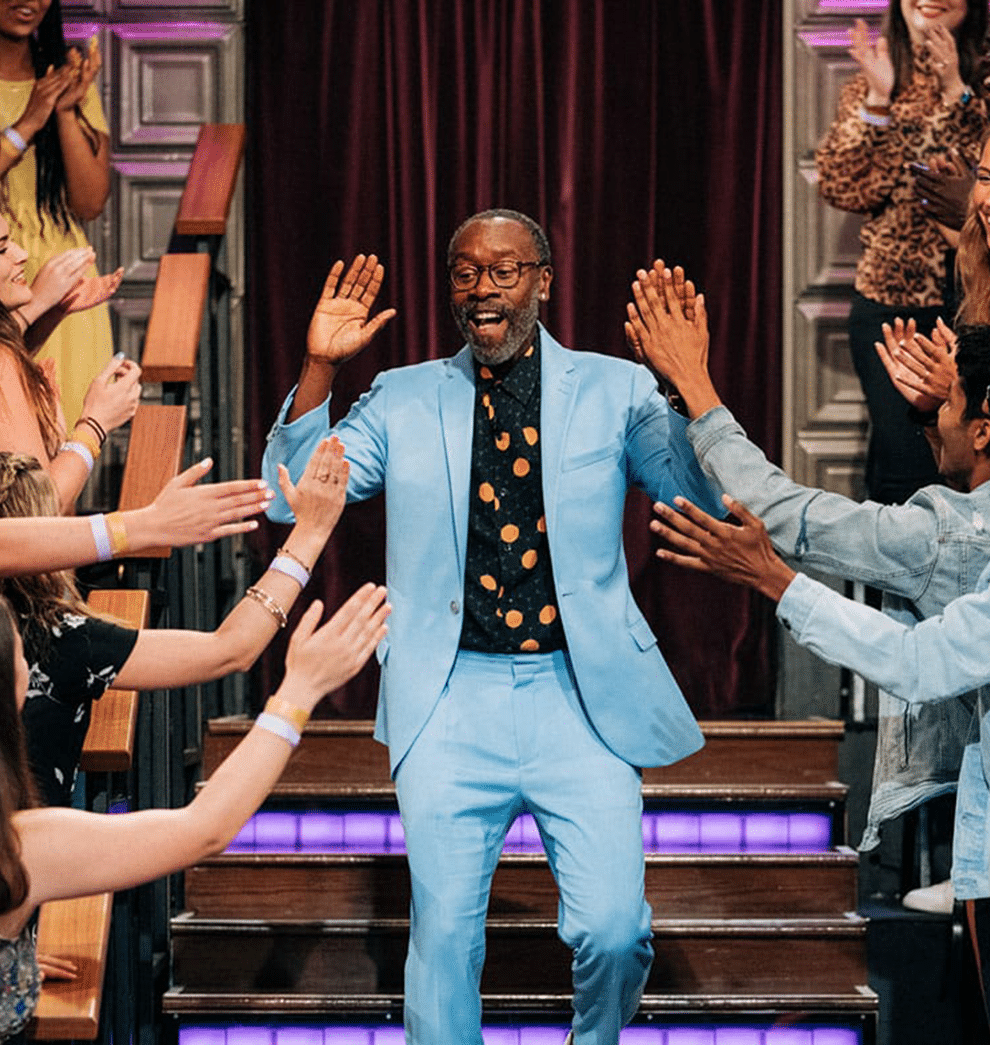 Don Cheadle in blue suit steps down stairs while high-fiving audience members