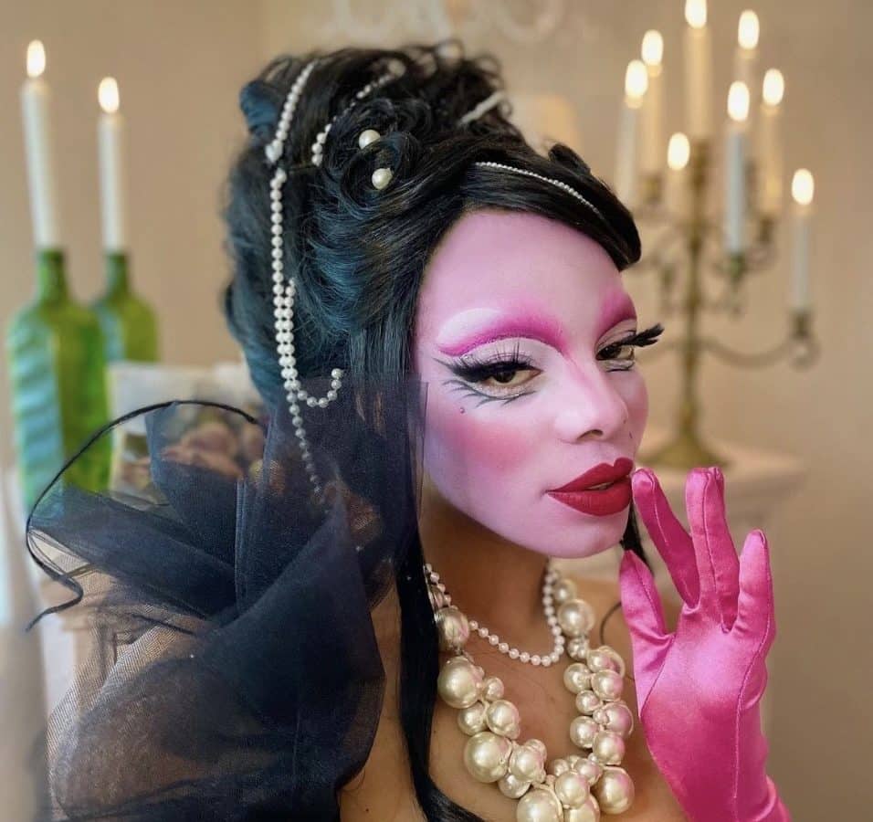 Jasmine Sugar wears pink opera gloves, a large pearl necklace, and bright pink drag makeup