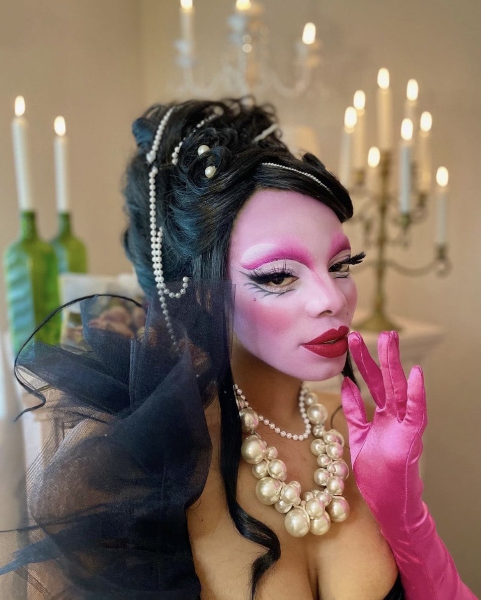 Jasmine Sugar wears pink opera gloves, a large pearl necklace, and bright pink drag makeup