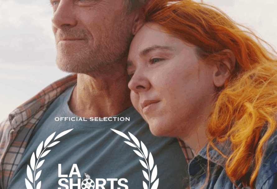 A close-up of a man and woman in a tender moment, with the man sporting blond hair and a beard and the woman having vibrant orange hair. Overlayed with "LA SHORTS" festival logo and the text "OFFICIAL SELECTION."
