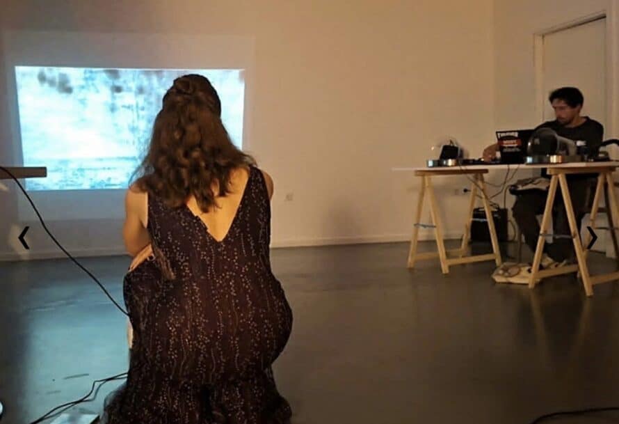 A woman kneels before a projection while a man operates equipment nearby.
